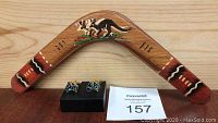 Small wooden boomerang painted with kangaroo and aboriginal style decorations, displayed behind two pairs of opal cufflinks shaped like Australia with gold-tone backings and MaxSold lot card.