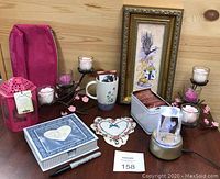 Photo showing entirety of self care lot: mug, framed lavender art, candles on metal holder, embroidered heart cloth, keepsake box, tea sachets tin, rotating light show with tulips, cosmetic bag, pink lantern, and black pen.