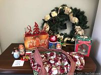 Full view of lot including Christmas fabric bag, wreath with ribbon and berries, three angel figurines, mini stocking, box with red metal candle holder, and assorted ornaments