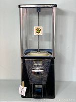 Front view of vintage gumball machine showing glass globe, metal base with coin slot and handle, and price sticker for 25 cents.