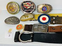 Top-down photo showing nine different vintage belt buckles alongside four belts in various colors including yellow, brown, and black.