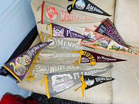 Collection of multiple vintage USA felt pennants arranged on a beige surface showing various locations and events including World’s Fair and several state/national landmarks.