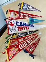 Eight vintage Canadian felt pennants laid flat and overlapping, showing text and graphics for Cobalt, Upper Canada Village, Moosonee, Canada 1976 Olympics, Ste Anne De Beaupre, Kirkland Lake, Quebec, and Old Fort York Toronto.
