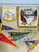 Overview of the collection showing the Mexico 1968 Olympics mini pennants, Caribbean destination pennants, and a Niagara Falls Canada pennant with fringe and flags.