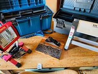 Wide view showing LED light, blue Rubbermaid tool box, gray tool box, wooden round die set, metal wood planer, oil filter remover, and metal stool.