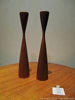 Pair of mid-century teak candlesticks shown upright on wood table, displaying their tapered hourglass shape.