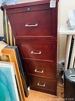 Front view of the tall dark wood filing cabinet showing the four drawers with metal handles.