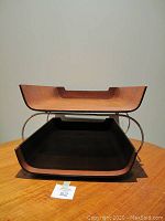 Front view of two teak trays stacked on the metal stand showing curved profiles and handles.