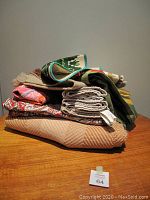 Stack of assorted handwoven wool placemats and printed linens in various colors and patterns