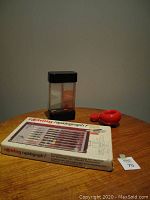 Photo of Rotring Rapidograph F pen set in original packaging, vintage op art desk toy with black base and top, and red Danish wooden nutcracker sculpture.