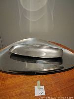 Large oval Alessi tray with a smaller elongated pewter dish on top, shown from an overhead angle on a wooden surface