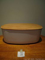 Front view of a white acrylic bread box with a bamboo lid on a wooden surface.