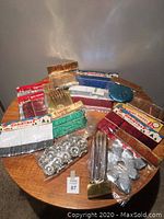 Photo of assorted Japanese vintage holiday decorations on round wooden table, mostly in original plastic packaging, showing colorful foil fringe garlands, twist tinsel, silver tinsel clusters, and metallic candle clips.