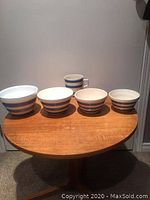 Four blue and white striped nesting bowls and a large mug placed on wooden table.