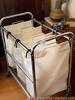 Full angled view of the laundry cart with three hanging beige fabric bags and stainless steel frame.