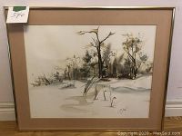 Framed original watercolor artwork depicting a winter landscape with bare trees and minimal ground cover. It is mounted with a beige mat and framed with a thin metal frame, no glass present.