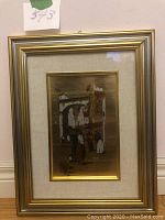 Framed artwork front view showing gold foil background with street scene illustration and gold frame.