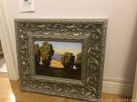 Front view of oil painting and ornate frame against wall