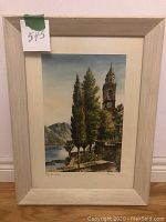 Framed original watercolour painting of bell tower by the lake leaning against the wall.
