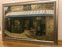 Full view of framed oil painting showing French restaurant exterior with green facade and striped awning.