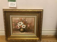 Framed oil painting of white and pink flowers with orange accents in a gold vase, ornate gold frame, displayed on wall.