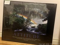 Framed motivational poster titled "Attitude" showing full view of poster with waterfall, rainbow scene and quote, glass cover reflecting surroundings.