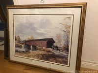 Framed limited edition print of 'The Last Covered Bridge' by Peter Etril Snyder leaning against a wall.