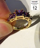 Angled view held by fingers showing three princess cut amethysts in prong settings
