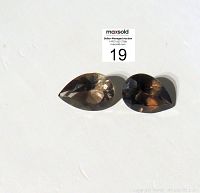 Two teardrop shaped smoky quartz gemstones placed side by side on a white surface under natural light, showing their color and faceting.