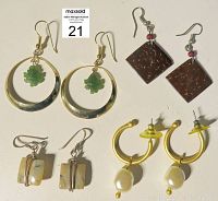 All four pairs of vintage earrings shown arranged flat on a light surface. Includes a pair with jade leaf pendants, brown square earrings, gold-tone hoops with pearl drops, and shell-like rectangular dangles.