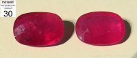 Two oval bright red ruby gems placed side by side showing color and visible minor inclusions