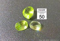 Three faceted pear-shaped peridot gemstones shown on a dark surface alongside a lot card.