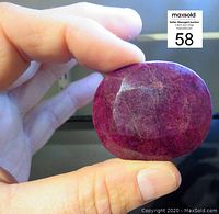 Hand holding oval faceted ruby, showing shape, color and size relative to hand