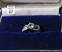 Blue topaz silver ring in a blue velvet jewelry box, showing the top and front of the ring with the center round blue topaz gemstone and the split band with small clear stones.