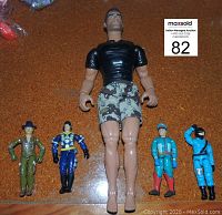 Five vintage G.I. Joe action figures laid flat, including one larger 12-inch figure and four smaller figures all in various military-themed outfits