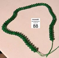 Full view of the 15-inch green faceted emerald bead necklace laid out in a full strand on a white surface.