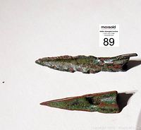 Top-down and angled view showing two bronze arrow points with green and reddish copper tarnish. One serrated, one smooth with hole near base.