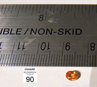 Orange sapphire gemstone placed next to a ruler showing size around 6 mm in length.