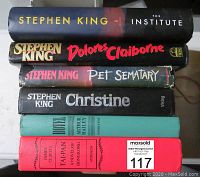 Stack of seven hardcover books showing spines with titles by Stephen King and others, including a MaxSold auction sticker on one book.