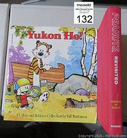 Front cover of the 'Yukon Ho!' Calvin and Hobbes comic book resting on top of the 'Peanuts Revisited' book with a visible red spine.