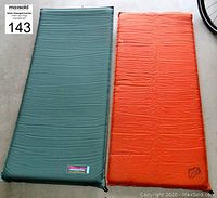 Two half-length inflatable camping pads side-by-side on the floor, one green and one orange, showing full length and condition.