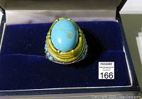 Close-up front view of vintage ring with large oval turquoise stone, gold-tone accents, and turquoise beaded decoration in a box.