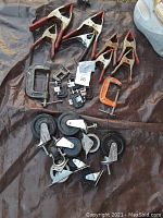 Photo showing the 7 alligator clamps with rust and red handles, 7 C clamps including one orange, and 10 caster wheels grouped on a surface.