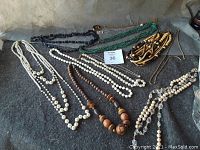 All 9 necklaces laid out on a dark surface showing various bead sizes, colors, and styles including pearl-like beads, wood beads, and chain styles.
