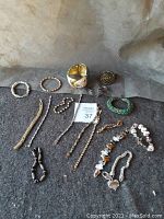 All 16 assorted bracelets arranged on a gray felt surface, showing various styles including clamp, hooked, and slide-on with different stone colors and metal finishes.