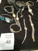 12 assorted costume watches laid out on black surface showing different band styles and faces