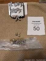 Full view of the eight pairs of earrings on a display card and a plastic bag containing multiple earring backs of various types.