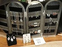 Photo of multiple pairs of earrings and some necklaces on a black plastic display stand.