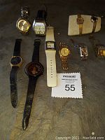 Top view of 10 wristwatches in varying styles and bands arranged on a dark surface.