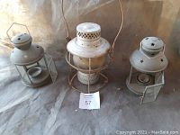 Three old metal lanterns with hinged glass doors open and star-shaped vents on top, showing rustic weathered finish and wire handles.